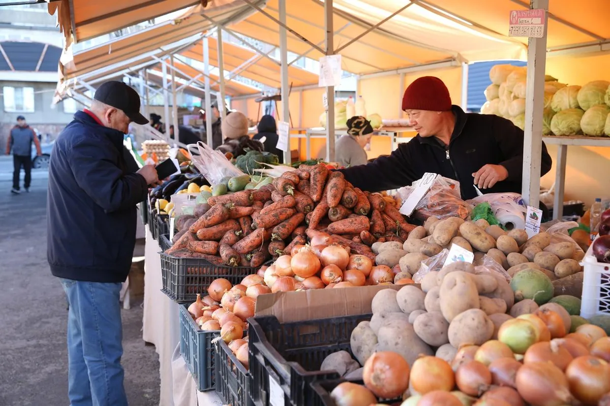 Покупатели выбирают свежие продукты на оживленной ярмарке выходного дня в одном из районов Алматы.