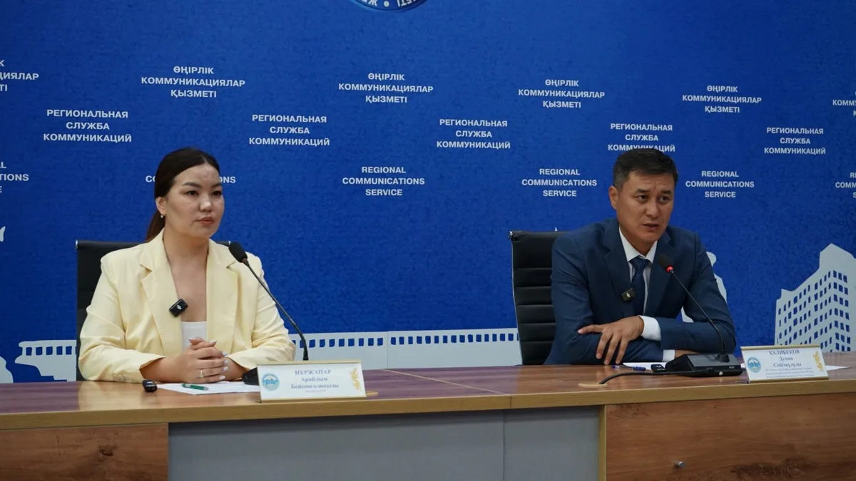 Рабочий проверяет водопроводную трубу в Жетісу на фоне нового строительства, символизируя модернизацию инженерных сетей.