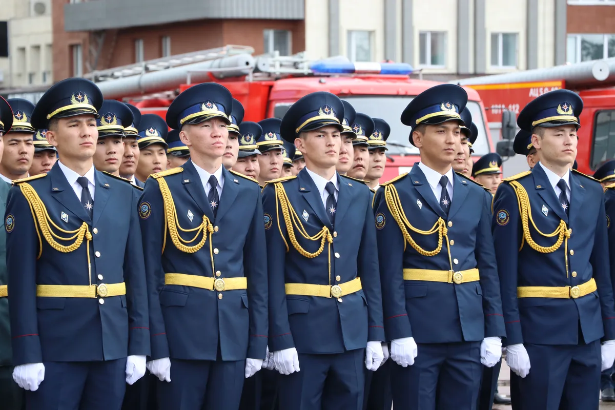 Сотрудники МЧС Казахстана в форме стоят перед зданием, готовы к выполнению служебных обязанностей.