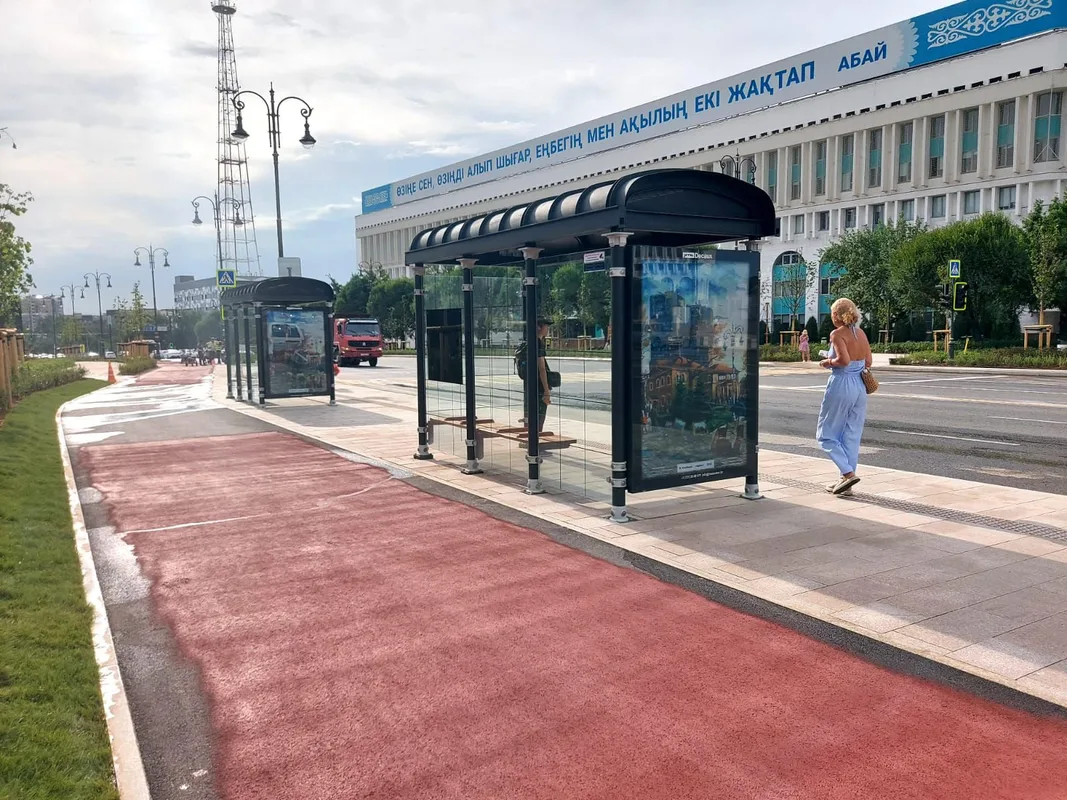 Новая автобусная остановка в Алматы на площади Республики с современным павильоном и ожидающими пассажирами.