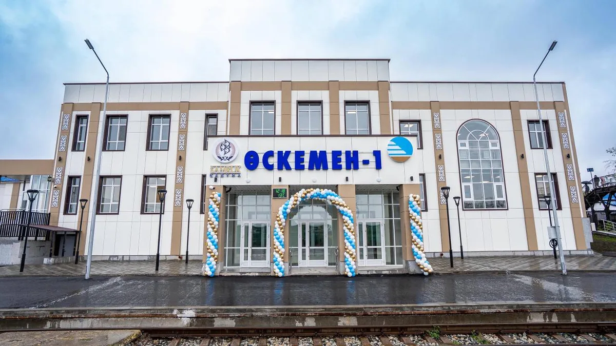 Фасад реконструированного железнодорожного вокзала Оскемен-1 в Усть-Каменогорске с новой вывеской и благоустроенной территорией перед ним.