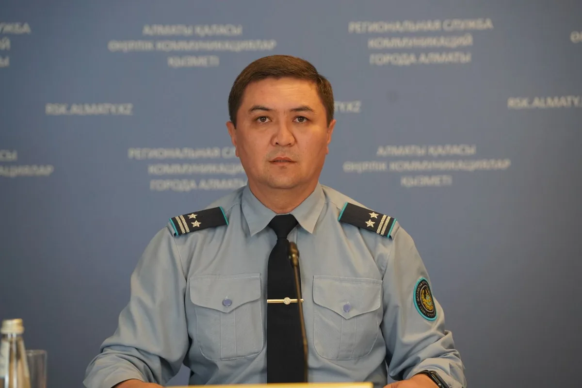 Сотрудник дорожной полиции регулирует движение транспорта возле школы в Алматы, помогая детям перейти дорогу.