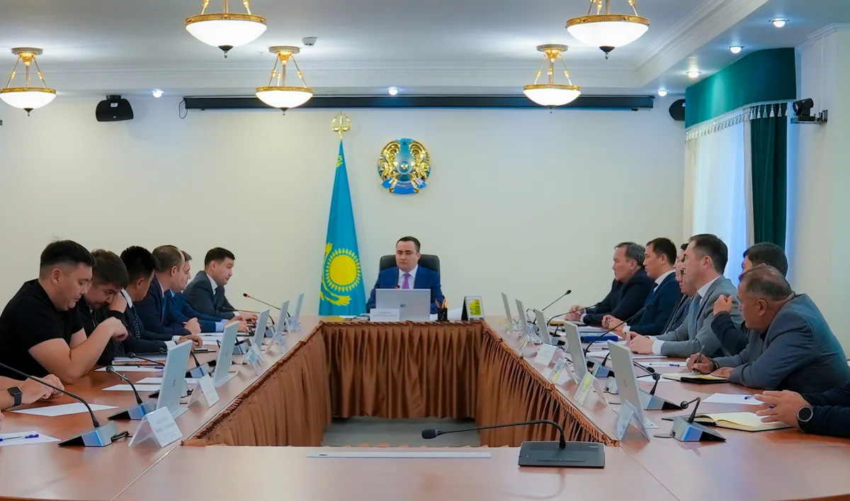 Рабочие на строительной площадке Астаны, на фоне видны башенные краны и строящиеся здания. Возможно, инспектор по труду проводит проверку.