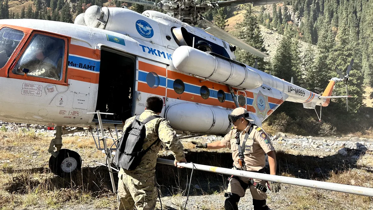 Панорамный вид на высокогорное моренное озеро в горах Казахстана, окруженное ледниками и каменистыми склонами, с голубой водой и следами инженерных работ.