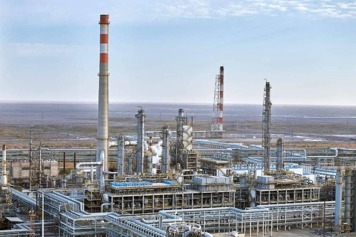 Индустриальный пейзаж Атырауского нефтеперерабатывающего завода с трубами и факельными установками, выпускающими дым.