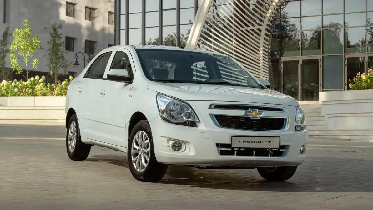 Обновленный седан Chevrolet Cobalt MCM белого цвета припаркован на улице, демонстрируя новый дизайн с хромированной радиаторной решеткой и затемненной окантовкой фар.