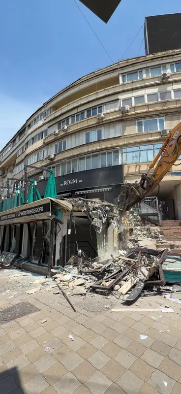 Демонтаж незаконно построенного здания в Алматы, на фоне городской застройки и жилых домов.